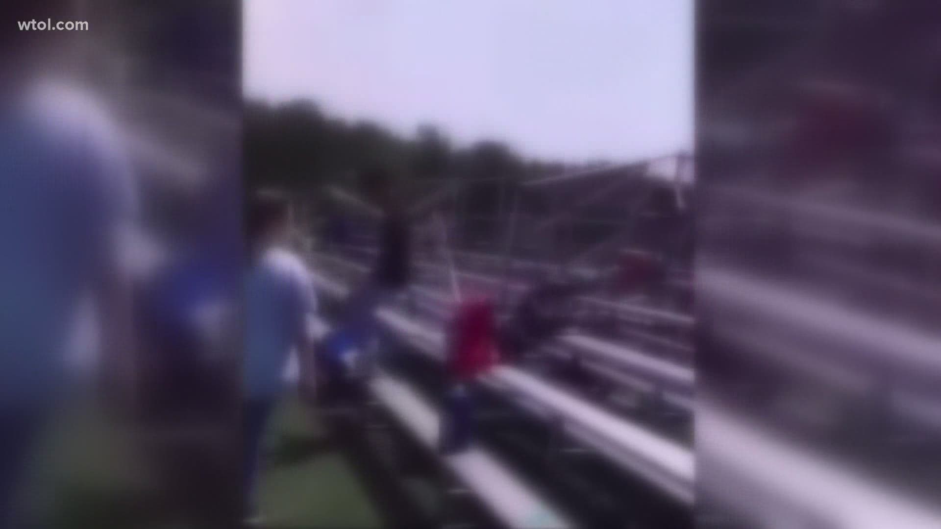 The video shows another student approaching the boy from behind, grabbing him and throwing him down against the bleachers while ripping a pride flag from his neck.